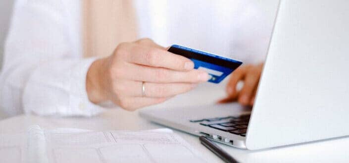 woman holding a credit card beside a laptop