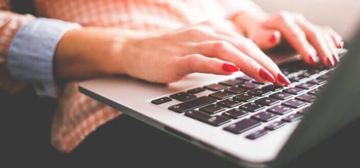 Polished fingers typing on a laptop keyboard.