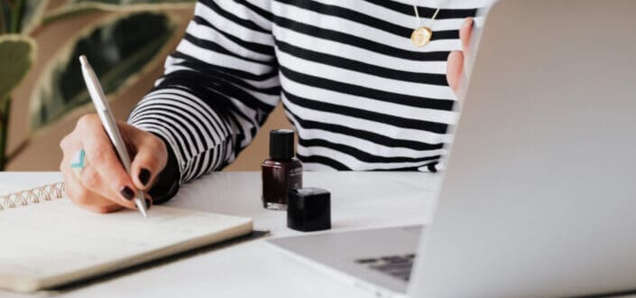 Woman writing notes facing her laptop