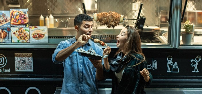 man feeding woman while standing in front of a food truck