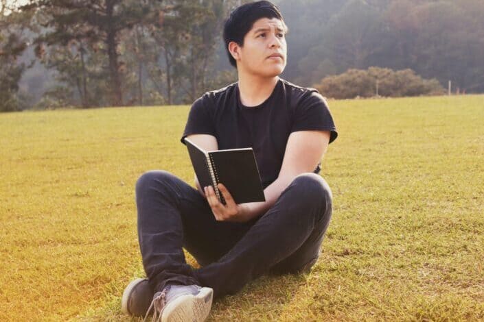 man with a notebook sitting on the grass 