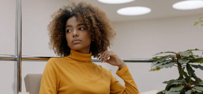 A serious faced woman wearing yellow turtle neck