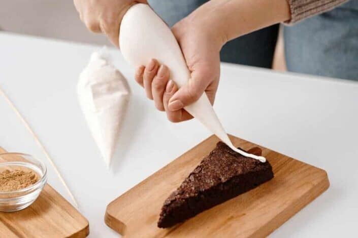 hand piping frosting into a slice of chocolate cake