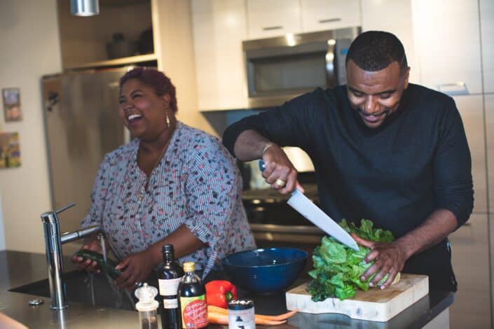 woman laughing and a man slicing a vegetable