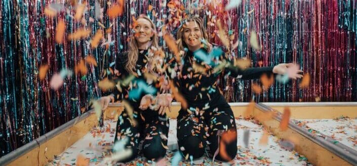 two women playing with confetti while kneeling