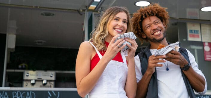 smiling man and woman eating take out food outdoors
