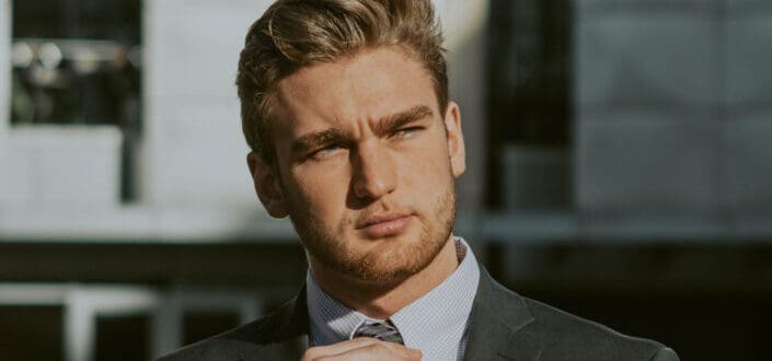 A guy wearing formal attire fixing his necktie