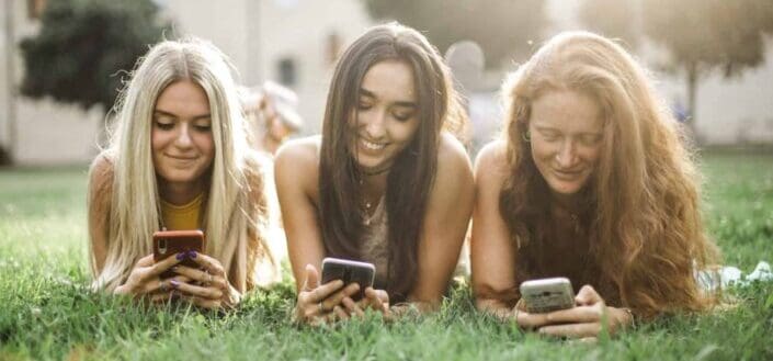3 female friends browsing smartphone on lawn