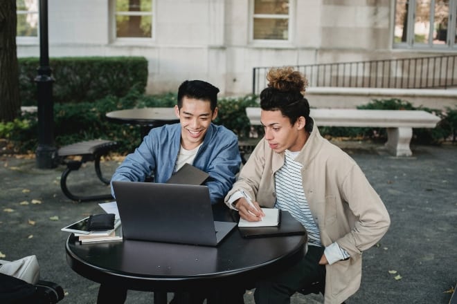 two people sitting in an outdoor table looking at laptop