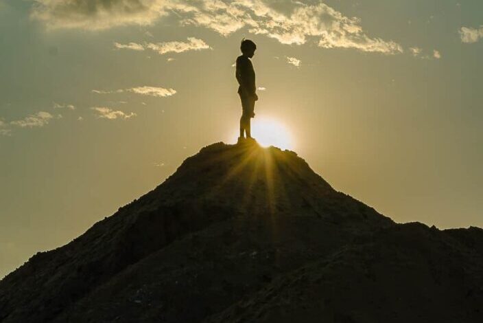 man on top a hill with sunset rays passing through him