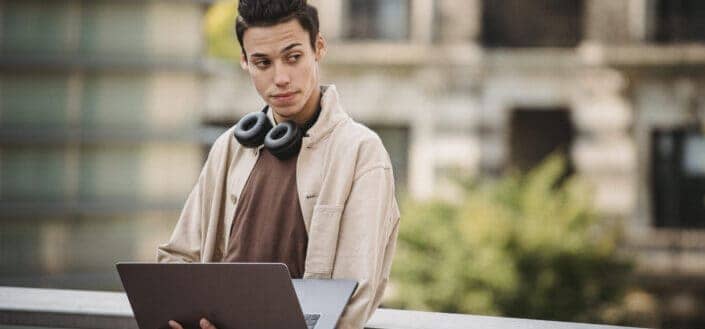 man looking at his side while holding a laptop and wearing headphones