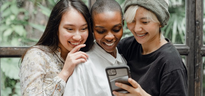 three women smiling while looking at a phone