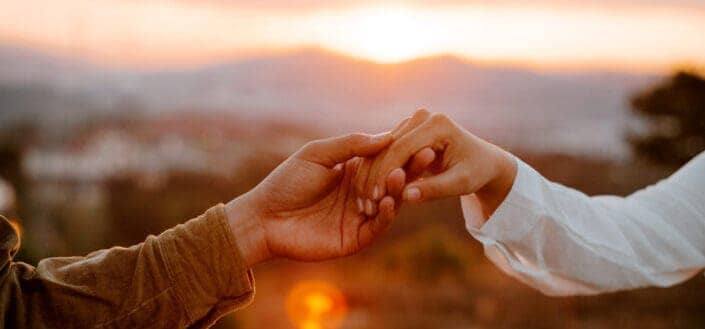 Unrecognizable couple holding hands at sunset