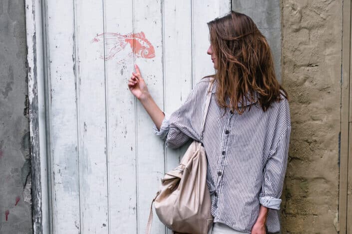 Woman wearing gray long sleeved shirt pointing at a fish painted on a white wall