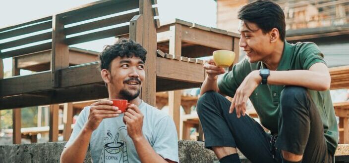 Two guys sipping coffee while sitting on wooden steps outdoors