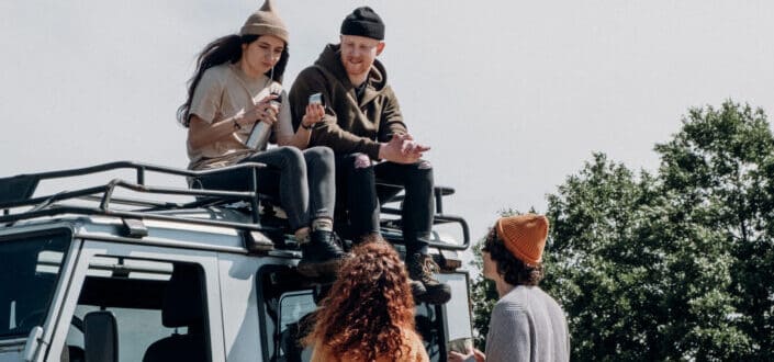 Two people sitting on roof of Jeep with two other people looking at them