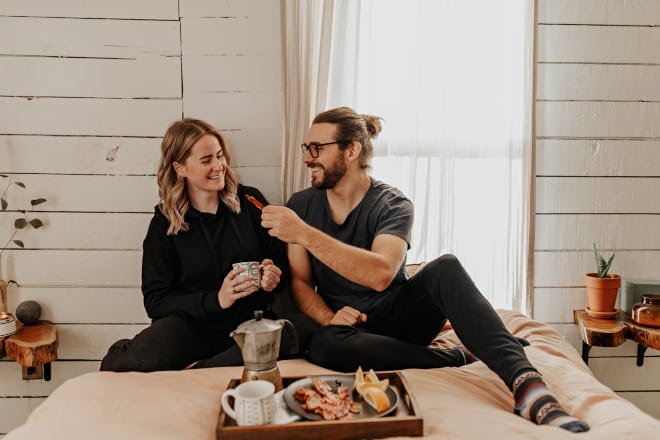 Young couple being playful while having breakfast in bed - Food pick up lines