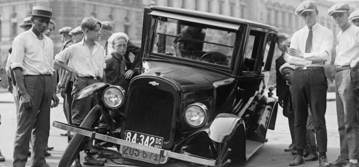 Old car with a flat tire drawing attention of a crowd