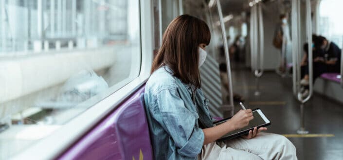 Girl sitting on train writing on her tablet