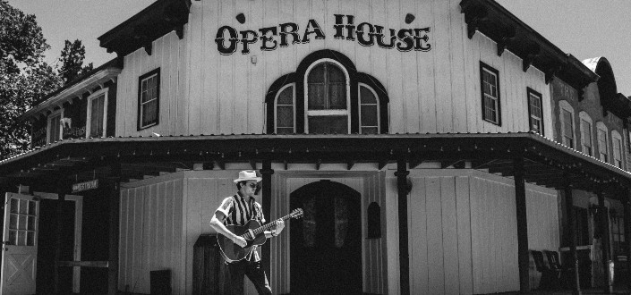 Man playing a guitar in front of an Opera House