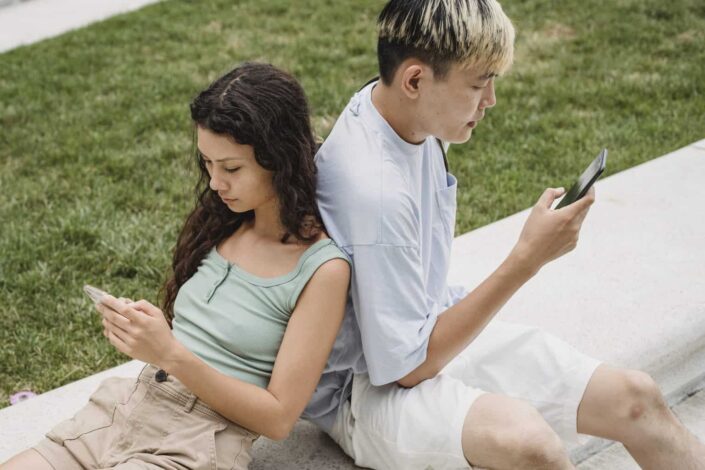 couple's leaning at each other' back while using phone