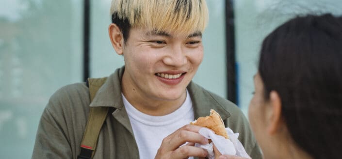 Cheerful guy grinning at girl while eating