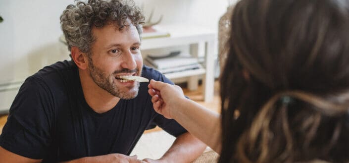 Happy man eating fruit from hand of wife