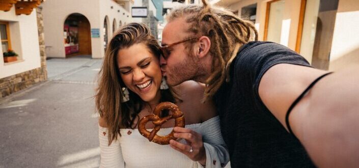 Woman holding pretzel being kissed by man