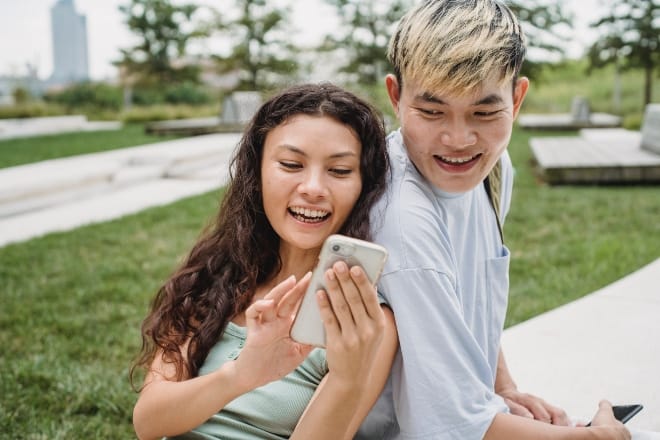 a couple smiling while scrolling a phone - tinder pick up lines