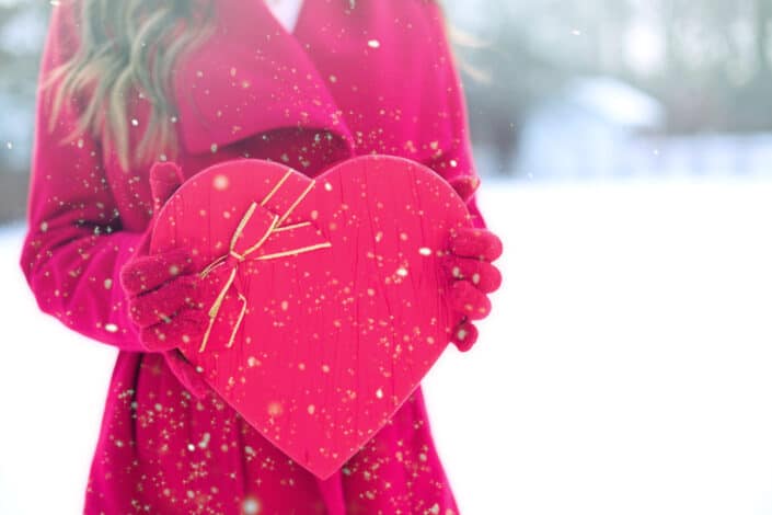 Woman in red coat holding heart shaped box.