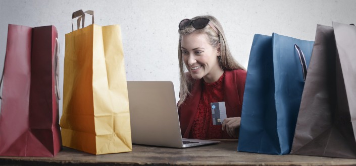 woman smiling at her laptop with shopping bags around her