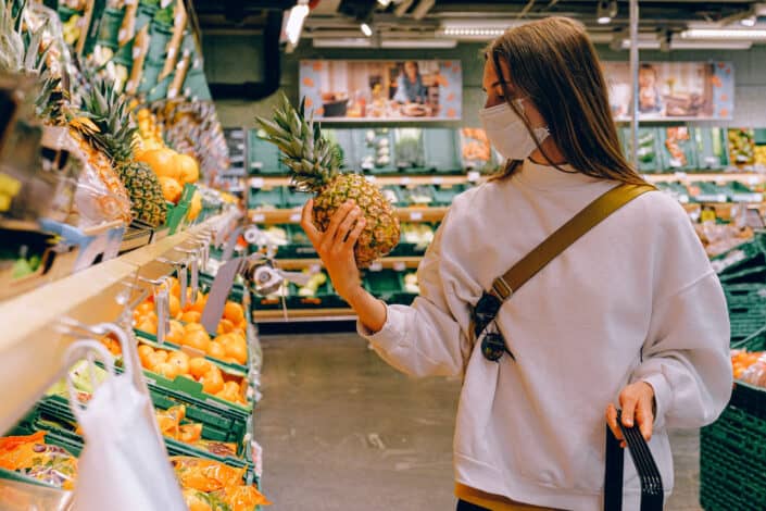 Woman wearing mask in supermarket holding pineapple 