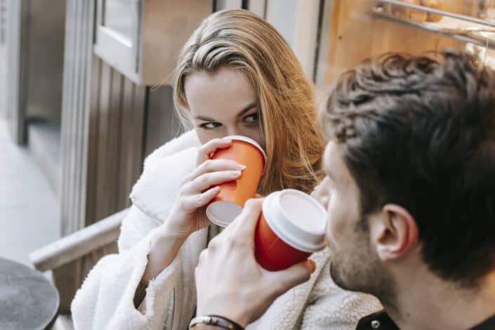 Young couple drinking hot beverages and looking at each other in cafe