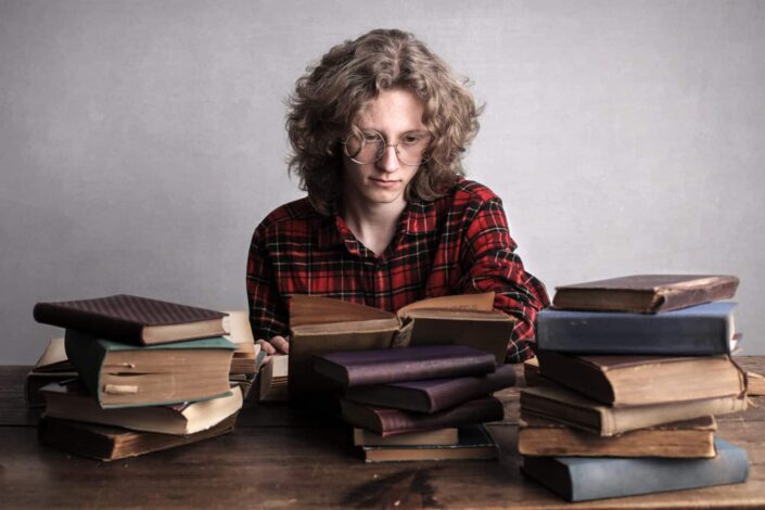 Person reading over pile of books on table.