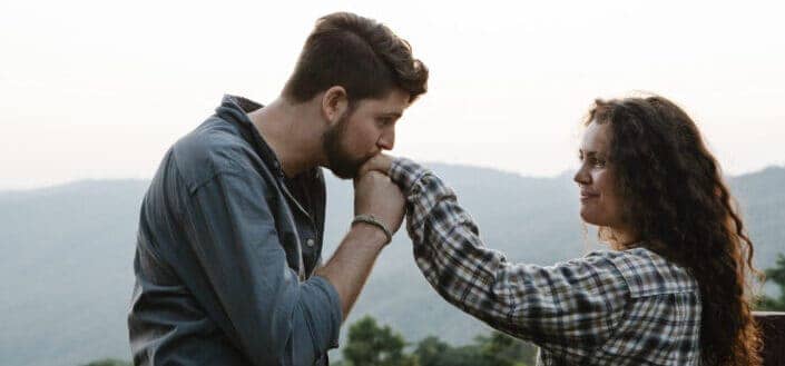 Young man kissing hand of smiling girlfriend in nature