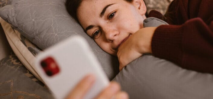 A woman lying in bed while checking her phone
