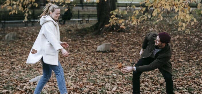 Cheerful young couple playing with fallen leaves in park