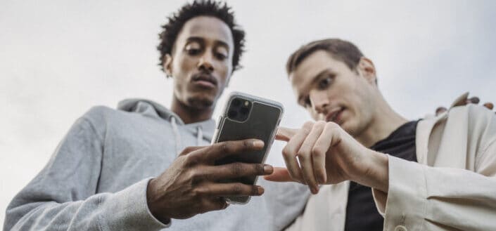 Multiethnic friends browsing smartphone together outside