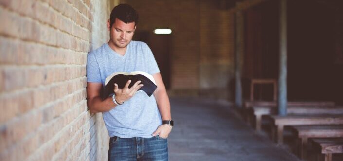 A guy casually reading while leaning on the wall