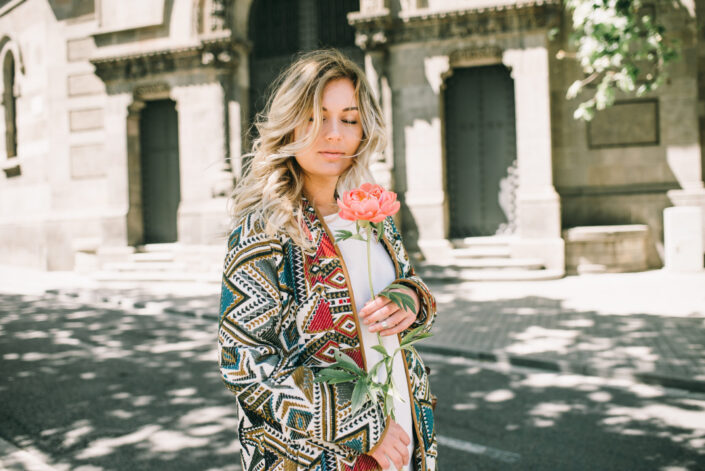 woman in tribal coat standing on street holding a flower