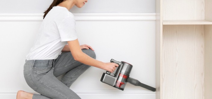 woman cleaning behind cabinet using an electronic tool