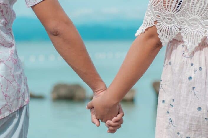 couple holding hands while facing the beach