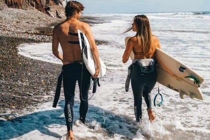 couple walking to beach, preparing to paddle out
