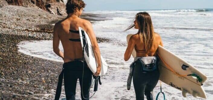 Surfer couple walking along the beach.