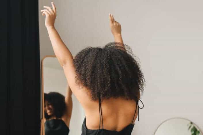 rejoicing curly haired woman looking herself in the mirror