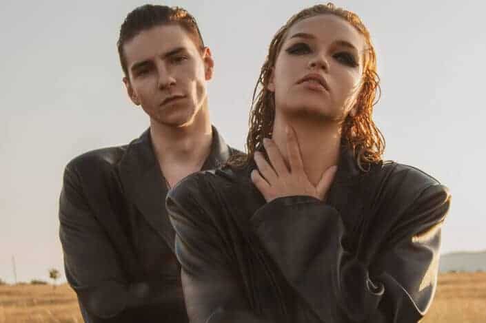 Stylish couple with similar leather cloaks in field