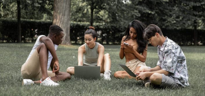 Diverse students with gadgets in park 