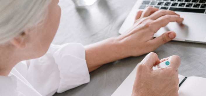 Elderly woman taking notes while using laptop