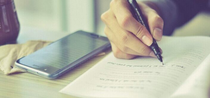 person writing a text from phone to notebook