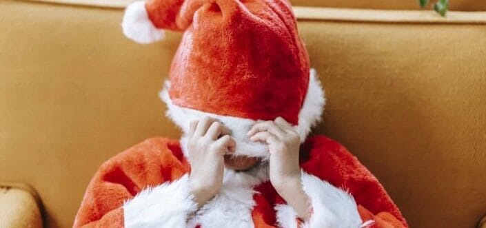 Little kid in Santa costume covering face 